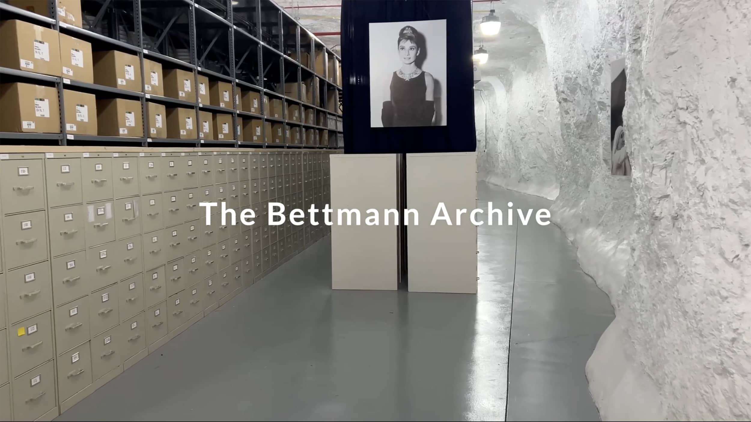 An image taken at the Bettmann Archive, with a photo of Audrey Hepburn, about to begin filming for Breakfast At Tiffany's hanging on the wall amongst shelves of archival materials.